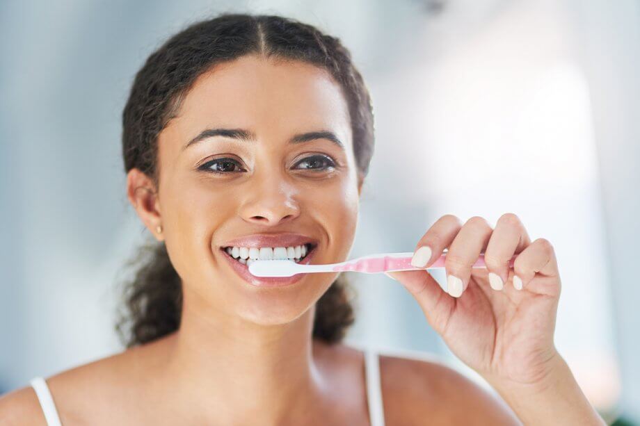 young woman brushing teeth with manual toothbrush