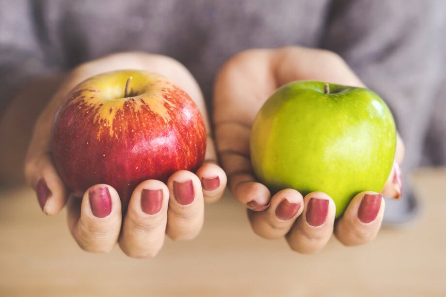 Woman holding a red apple in one hand and a green apple in the other. Only her hands and the apples are visible.