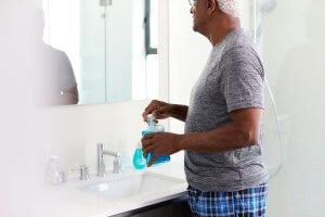 older man looking in bathroom mirror using mouthwash